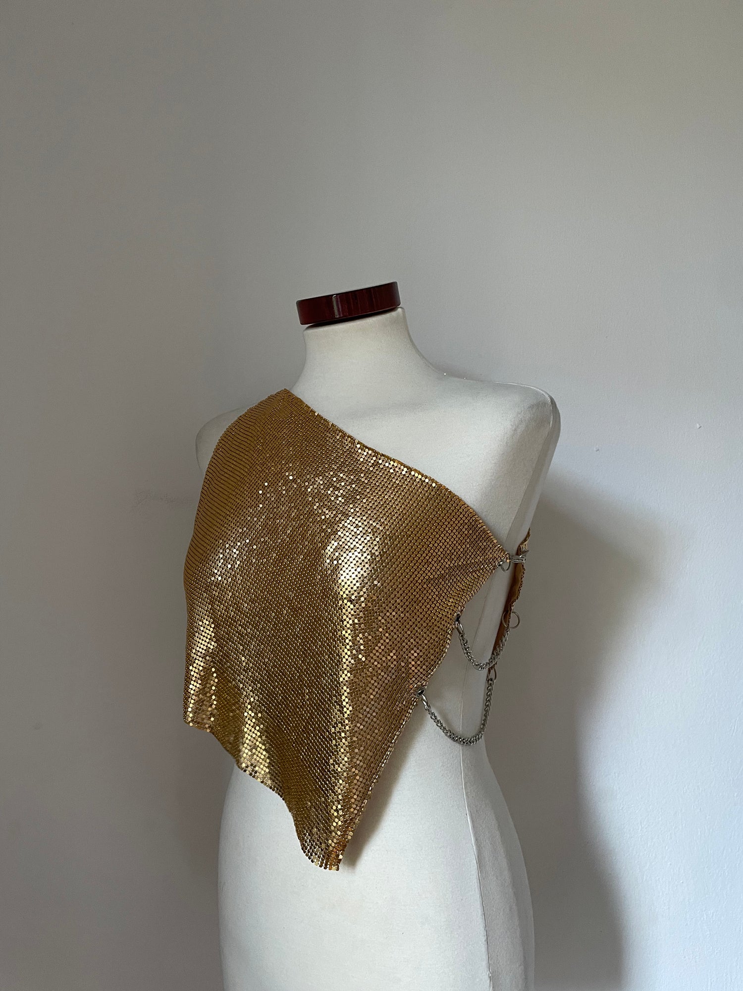 Model wearing a chainmail metal mesh top in color Gold. One shoulder with silver chains on the side.