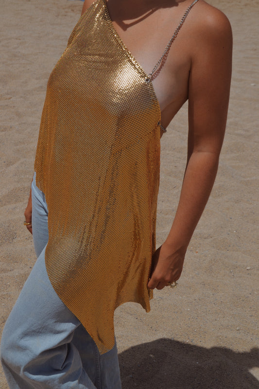 Model wearing an asymmetrical one shoulder chainmail top in gold. With silver chain straps.